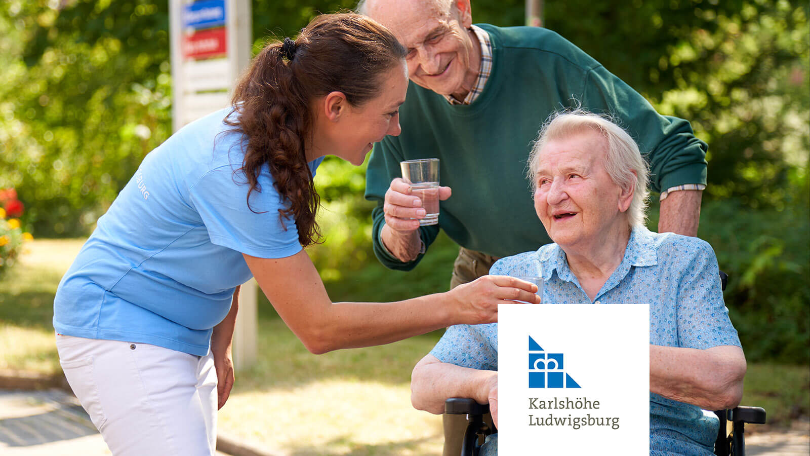 Eine Pflegekraft der Karlshöhe Ludwigsburg unterstützt zwei Senior*innen einfühlsam beim Trinken im Garten. Altenpflege, Betreuung und wertschätzende Unterstützung im Alltag.