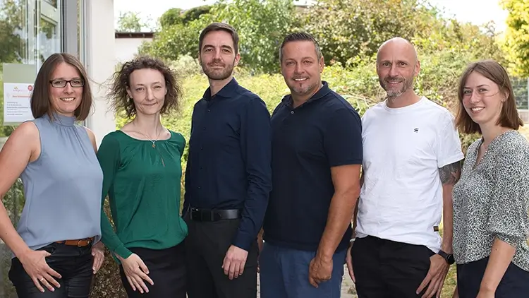 Klimazentrum Wolpertshausen - Gruppenfoto des Teams vor grüner Gartenkulisse, aufgenommen im Außenbereich einer Einrichtung.