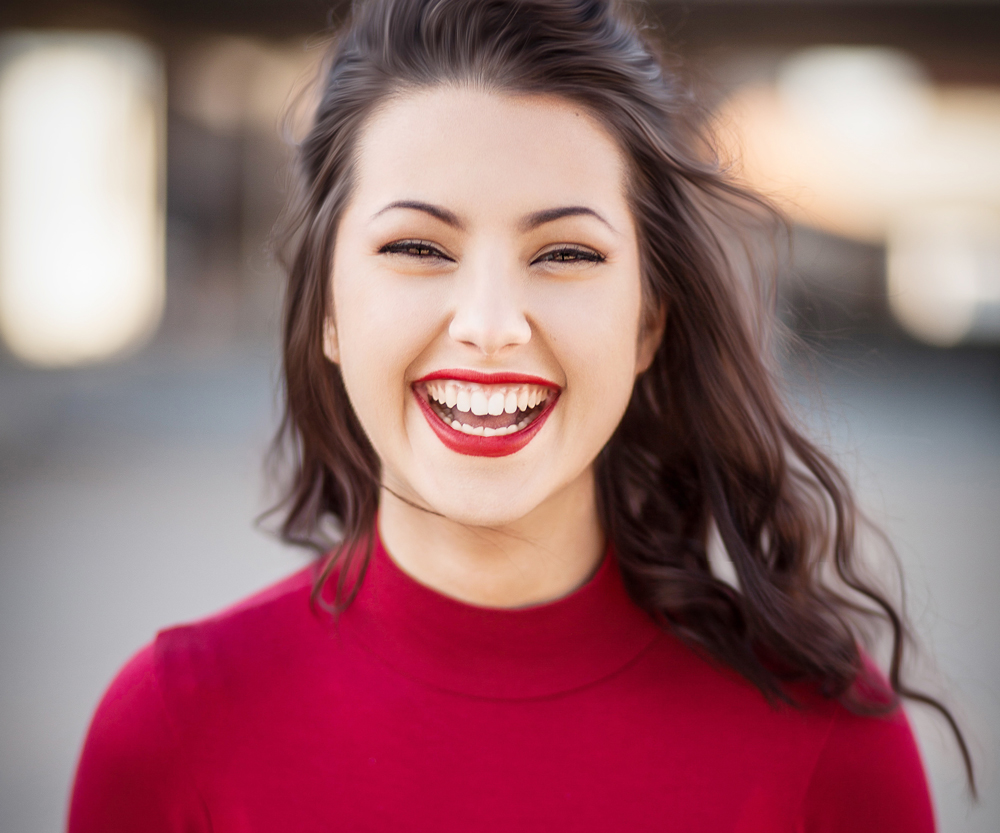 Lächelnde junge Frau mit strahlendem Ausdruck in einem roten Oberteil.