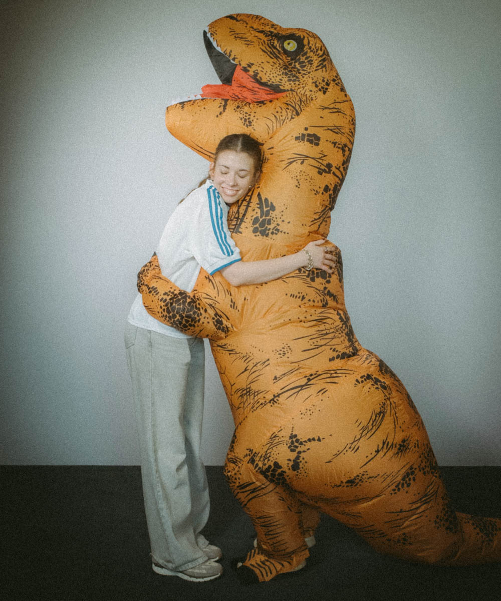 Eine junge Frau umarmt einen Menschen in einem Dinosaurierkostüm.