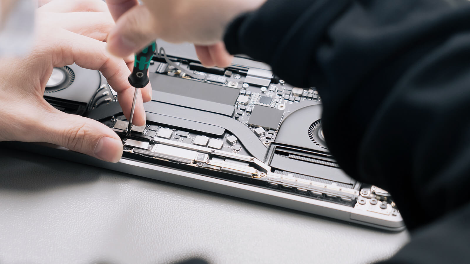 Nahaufnahme einer Hand, die mit Schraubenzieher an Laptop-Hardware arbeitet, Symbol für Handwerk und Technik.