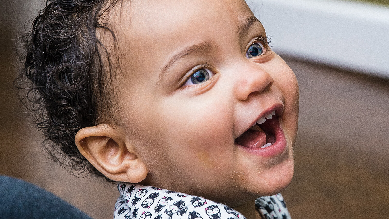Lachendes Kleinkind mit strahlenden blauen Augen, Symbol für Freude, Unbeschwertheit und Zukunft.