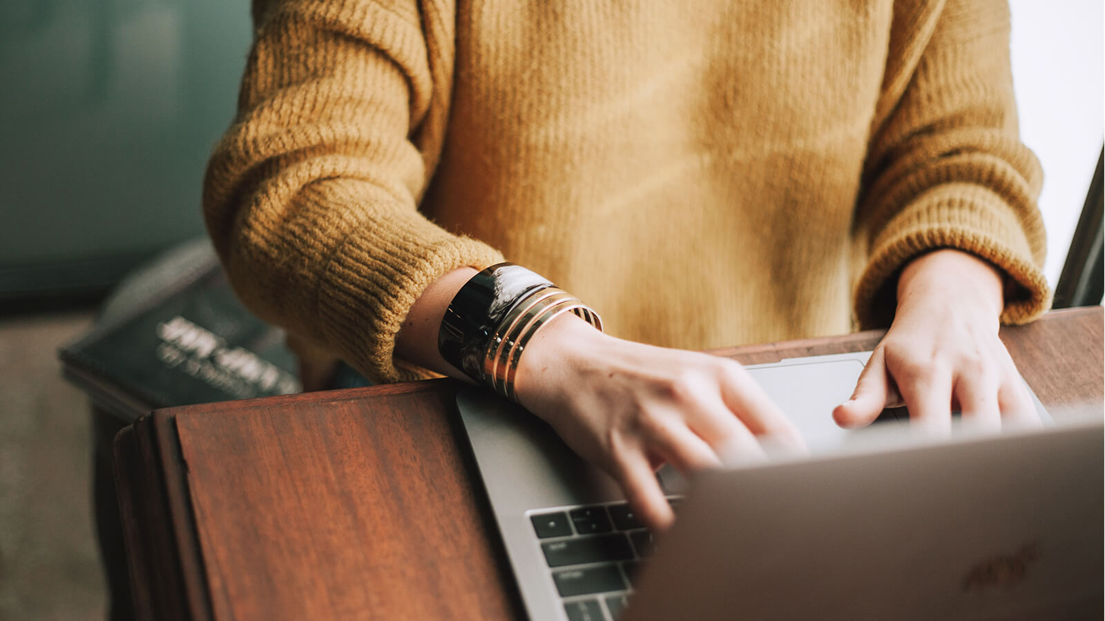 Frau tippt auf Laptop in gemütlicher Umgebung, Symbol für Kommunikation, Social Media und Öffentlichkeitsarbeit.